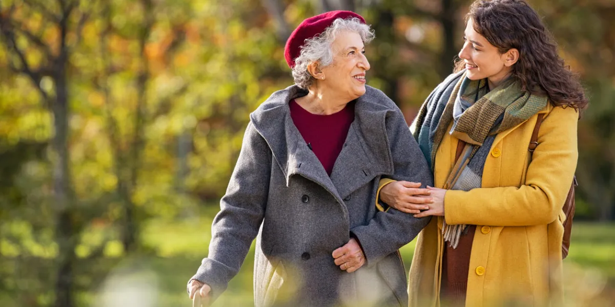 young woman in park wearing winter clothing walking with old grandmother happy grandma wearing coat walking with lovely girl outdoor with copy space smiling lovely caregiver and senior lady walking in park during autumn and looking at each other