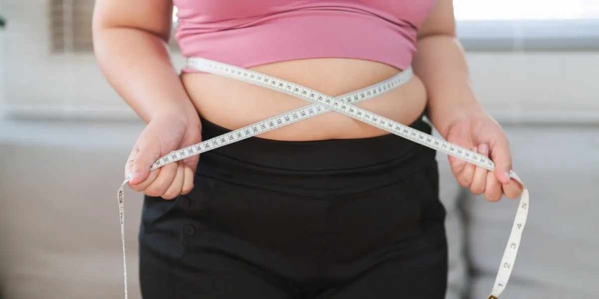 close up overweight woman measuring her hip with tape measure