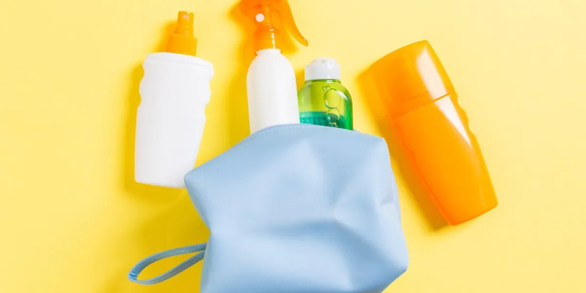 top view of female cosmetics bag full of suncream spray, sunsreen, sunblock and body lotion and spf cream on yellow background with copy space directly above bright summer concept