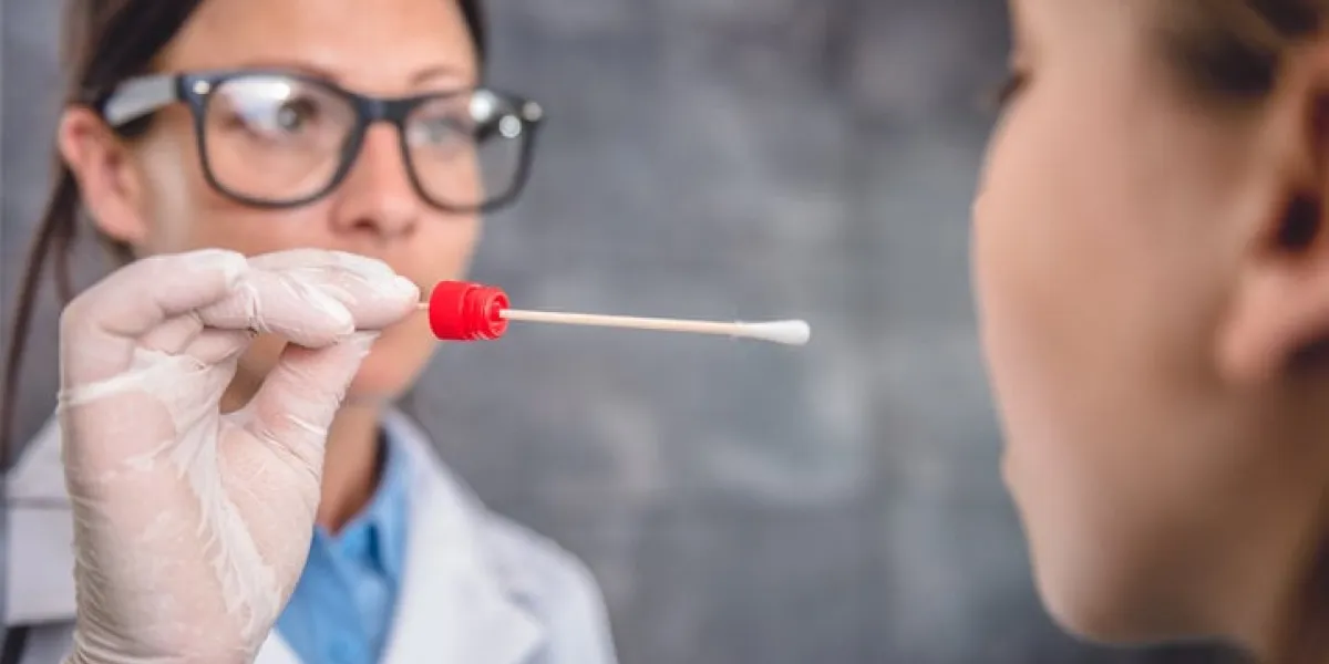 female pediatrician using a swab to take a sample from a patient's throat