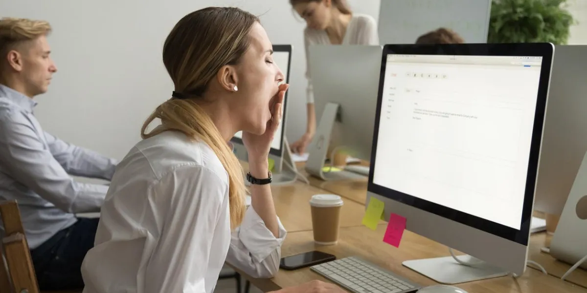 tired businesswoman yawning working on computer sitting at desk with colleagues, sleepy employee gaping suffering from lack of sleep, feeling bored or chronic fatigue in office concept, side view