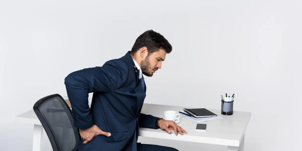 young businessman suffering from backache while sitting at workplace
