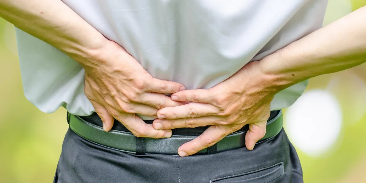 close up of a man holding his back in pain, isolated on white background, monochrome photo with red as a symbol for the hardening