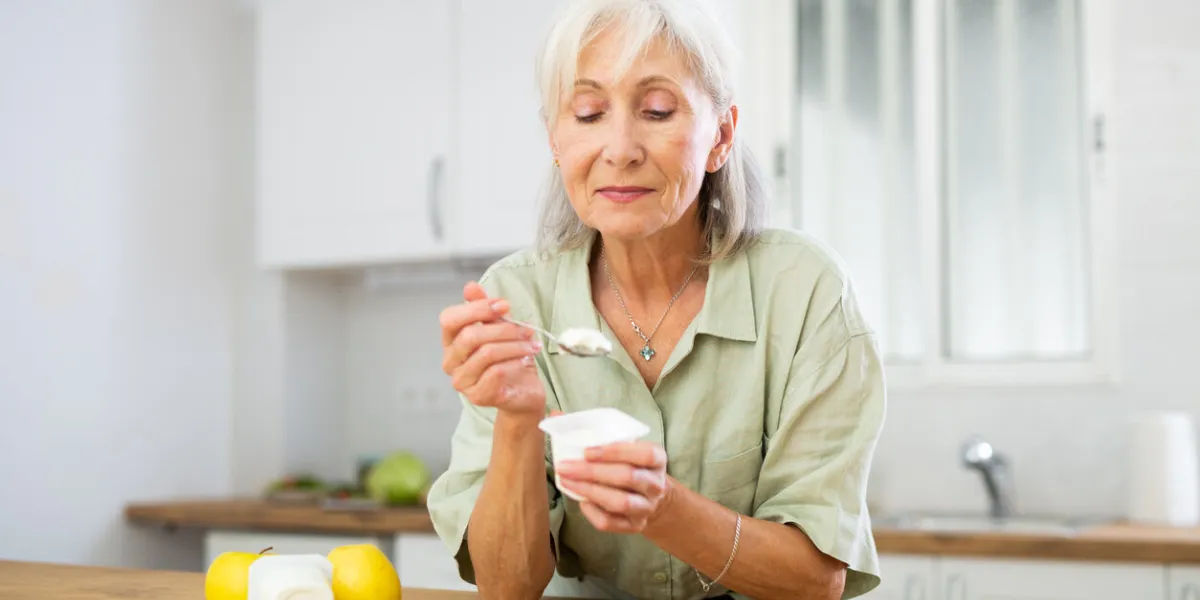 portrait of smiling retried woman enjoying yogurt as healthy snack in home kitchen