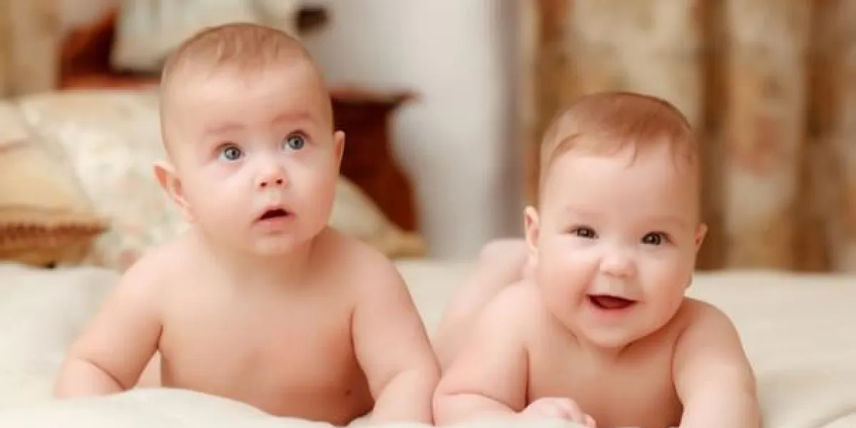 deux bébés jumeaux, filles souriantes de sept mois au lit sur des draps blancs