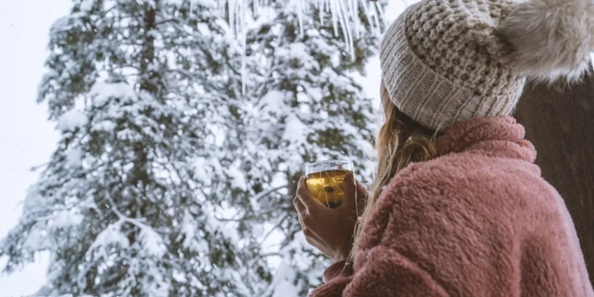 woman in log cain looking at the snow falling with tea cup in hands