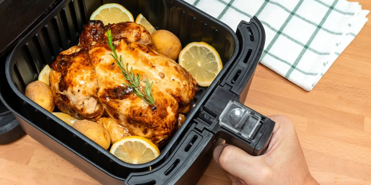 hand cooking whole roasted chicken with garnish in air fryer at the kitchen top view
