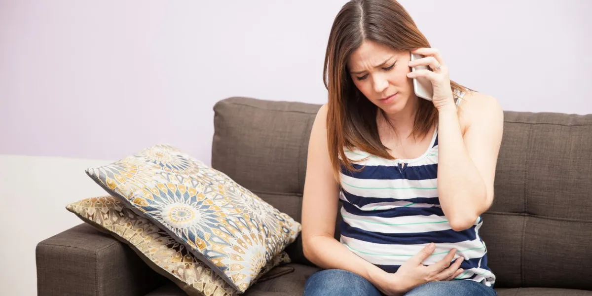 young pregnant woman feeling some pain and discomfort at home and calling her doctor