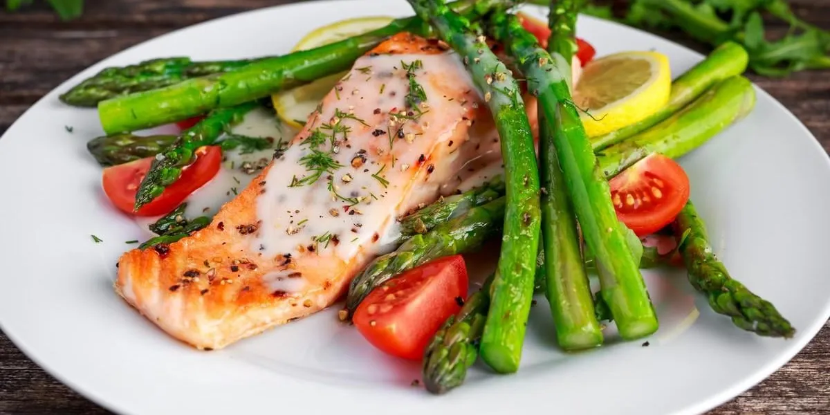 fried salmon with asparagus, tomatoes, lemon, yellow lime on white plate