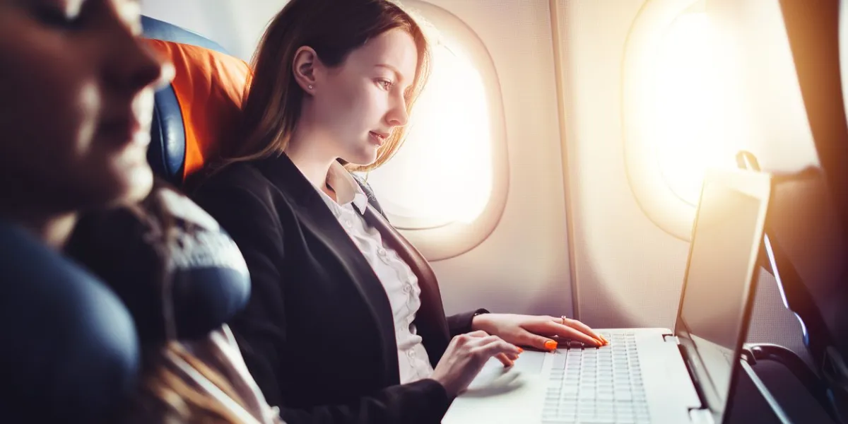 female entrepreneur working on laptop sitting near window in an airplane