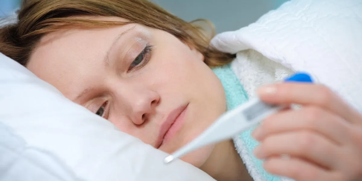 jeune femme couchée dans son lit avec un thermomètre