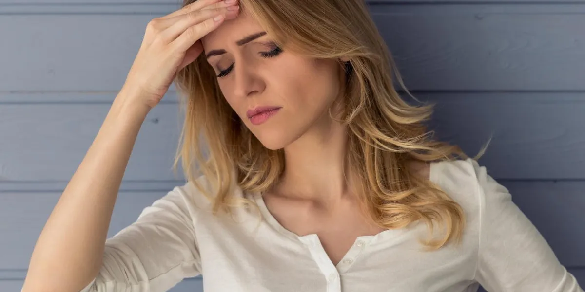 portrait de la belle jeune femme fatiguée ayant des maux de tête, gardant les mains sur la tête, contre le mur gris
