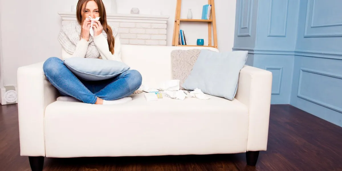 sick girl with fever sneezing in tissue sitting on sofa