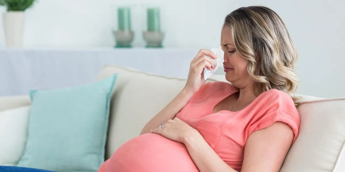 pregnant woman blowing her nose on the couch