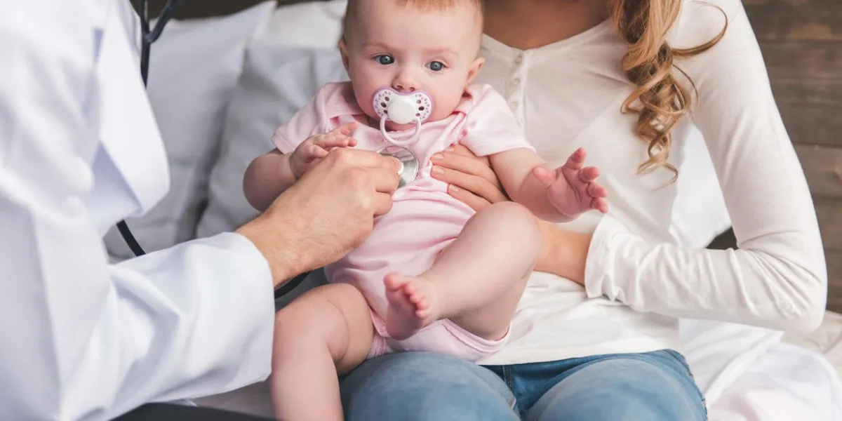 beautiful young mom is holding her cute baby while doctor is listening to baby's lungs