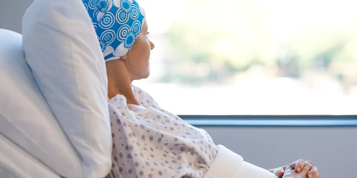 young woman in bed suffering from cancer thoughtful woman battling with tumor looking out of window young patient with blue headscarf recovery in hospital on bed