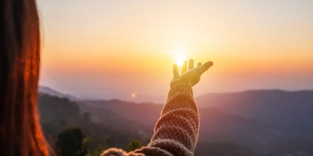 young woman hand reaching for the mountains during sunset and beautiful landscape