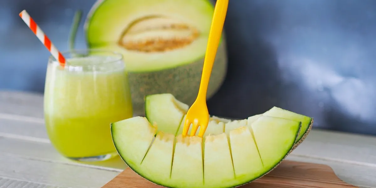 pieces of green net melon fruit or honeydew on wooden chopping board and a glass of melon juice for healthy eating or dietary food concept