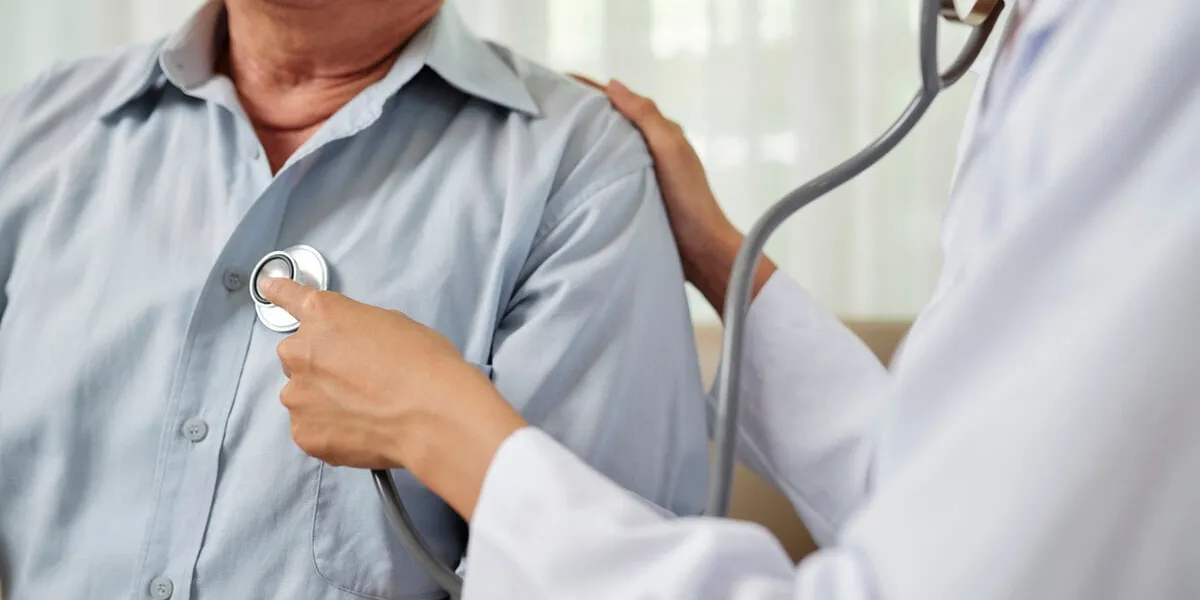 close-up of female doctor in white coat listening to breathe of senior man during his visit at hospital
