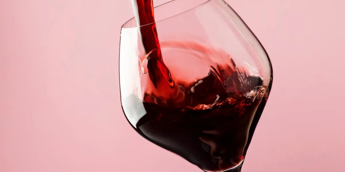 french dry red wine, pours into glass, trendy pink background, space for text, selective focus