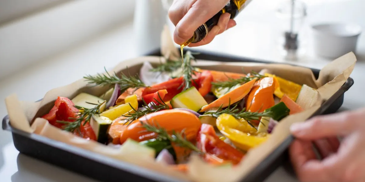 close up of seasoning tray of vegetables for roasting with olive oil ready for vegan meal