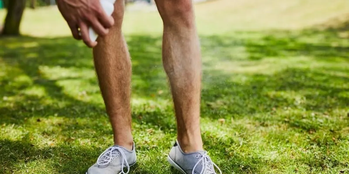 close-up of a man spraying insect repellent on his legs while outdoors