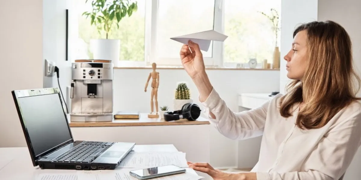 woman procrastinate at workplace freelancer on remote work at home office unmotivated tired woman play with paper plain lazy office worker