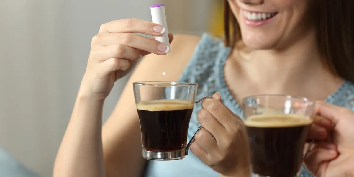 close up of a woman hand throwing saccharine into a coffee cup sitting on a couch in the living room at home