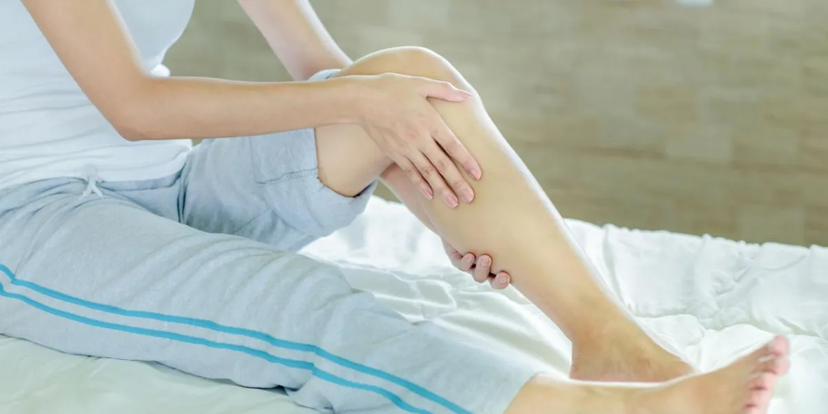woman massaging her leg on white bed
