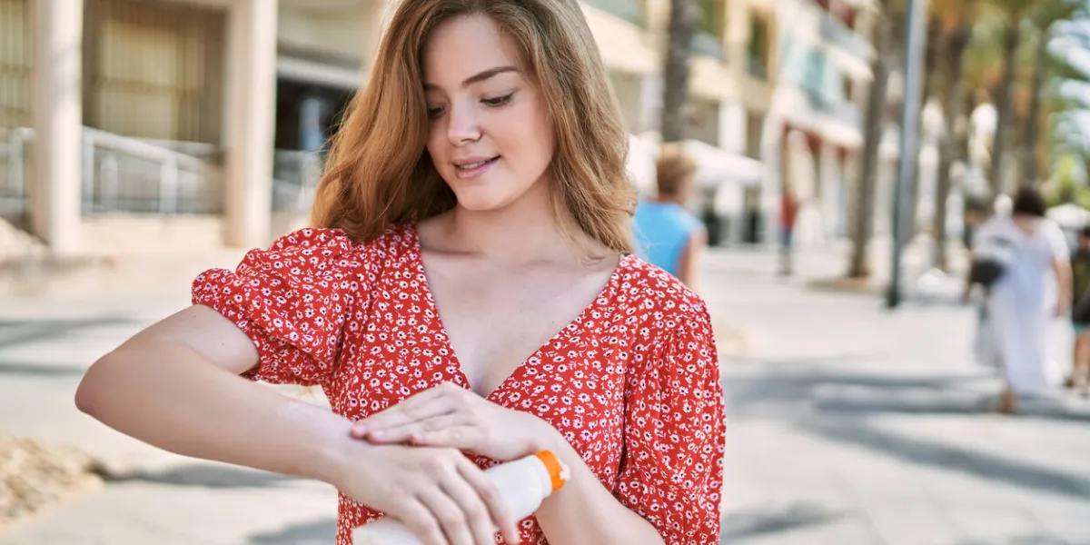 young caucasian girl smiling confident using sunscreen at street