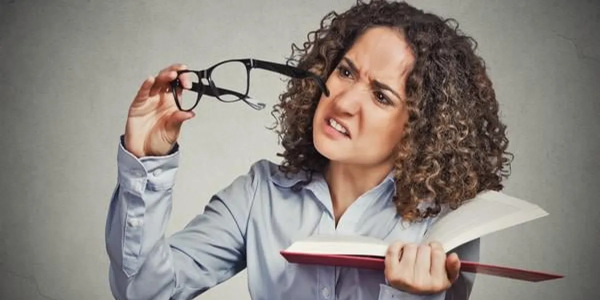 closeup portrait jeune femme, femme ne peut pas voir lire le livre a des problèmes de vision mauvais verres prescrit bouleversé isolé mur gris fond émotion humaine expression faciale, se sentir réaction de problème de santé