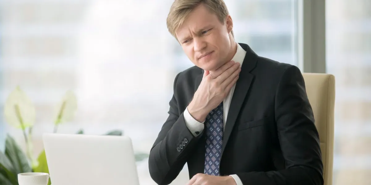 jeune homme d'affaires travaillant avec ordinateur portable au bureau dans le bureau, la main à son cou, se sentir mal, a mal à la gorge, après des cris, la perte de voix, l'irritation, la douleur et les démangeaisons, difficile à avaler
