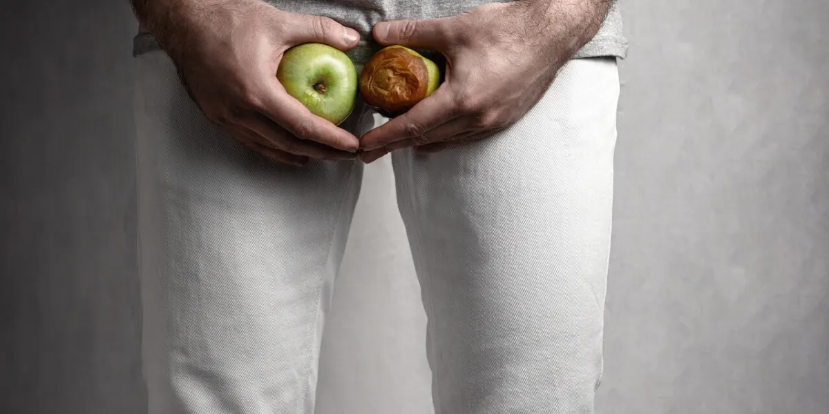 a man at the level of the genitals , holding a ripe and rotten apple male suffering with pain in the urogenital system the concept of protection of sexually transmitted infections close up