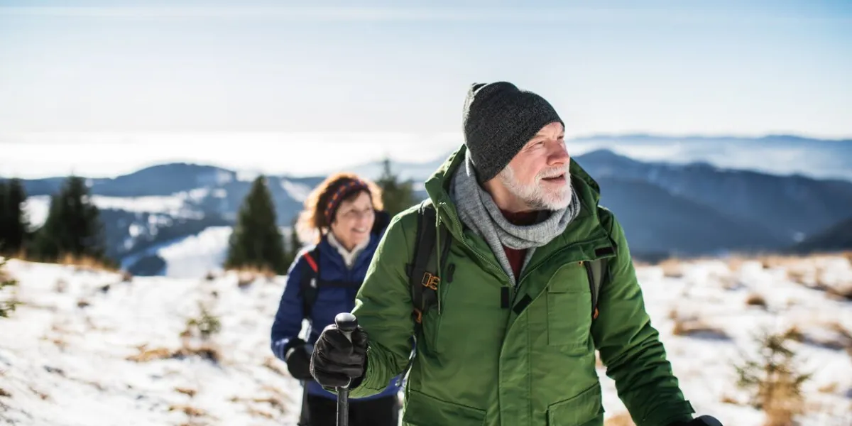 senior couple with nordic walking poles hiking in snow-covered winter nature, healthy lifestyle concept