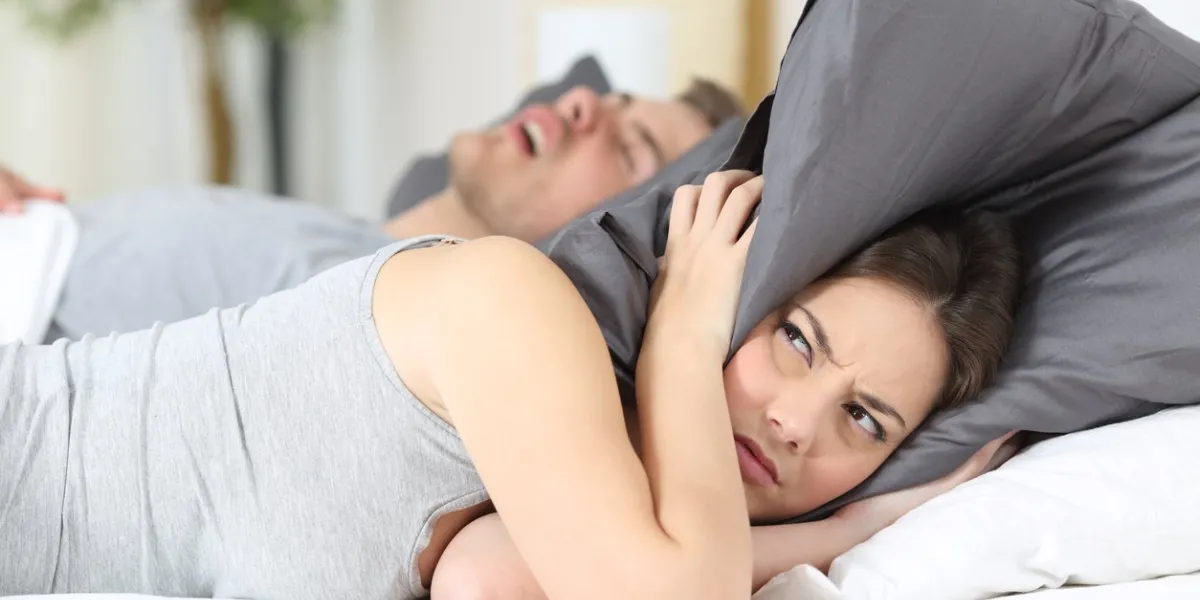 man snoring while his wife is covering ears with the pillow