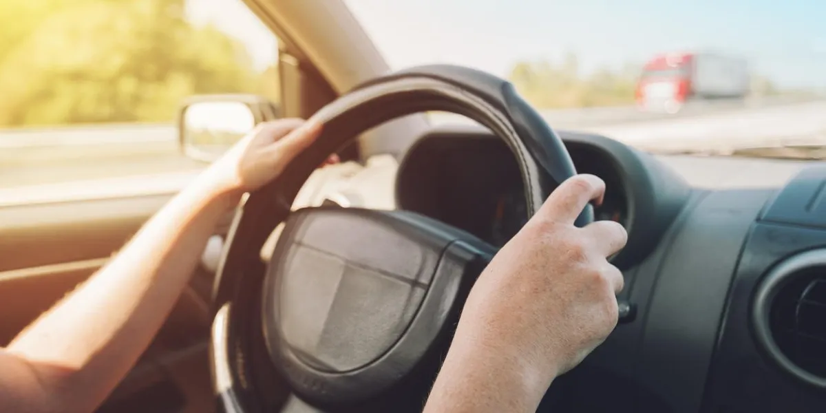 female hands holding on black steering wheel and driving car on motorway on sunny summer day