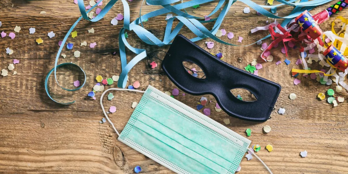 carnival 2020 party, coronavirus days, protective face mask and colorful confetti and serpentines on wooden background covid 19 spread prevention measure
