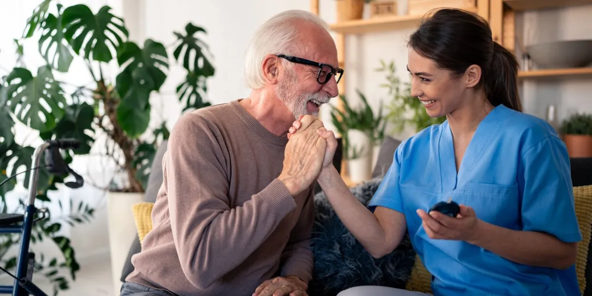 a cheerful female nurse in blue scrubs checks blood sugar levels for an elderly male patient at his home, reflecting attentive in-home medical care