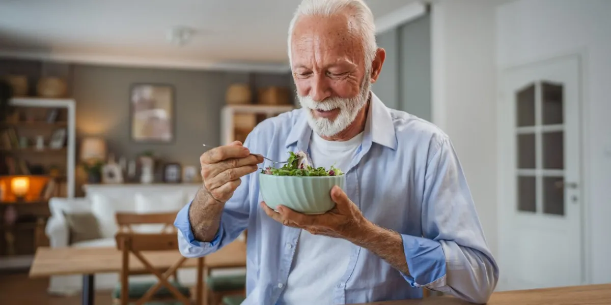 portrait of senior man stand at home and eat salad
