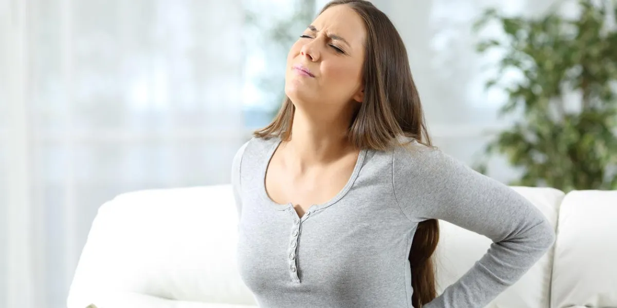 woman suffering back ache and complaining sitting on a couch in the living room at home