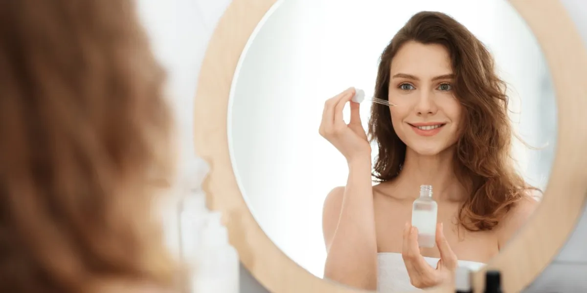pretty blonde woman applying serum on her face, home interior, daily beauty routine
