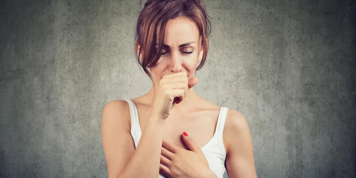 young woman having asthma problems and coughing badly covering mouth and holding hand on chest