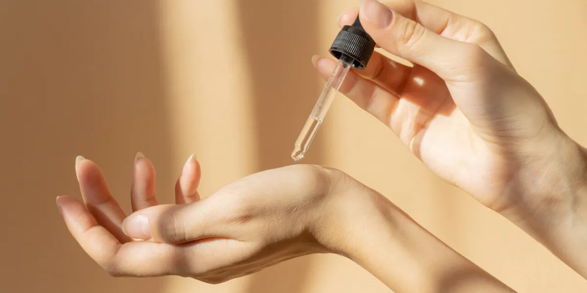 women's hands hold pipette with cosmetic serum on light brown background, in rays of sunlight close-up, copy space concept of body care