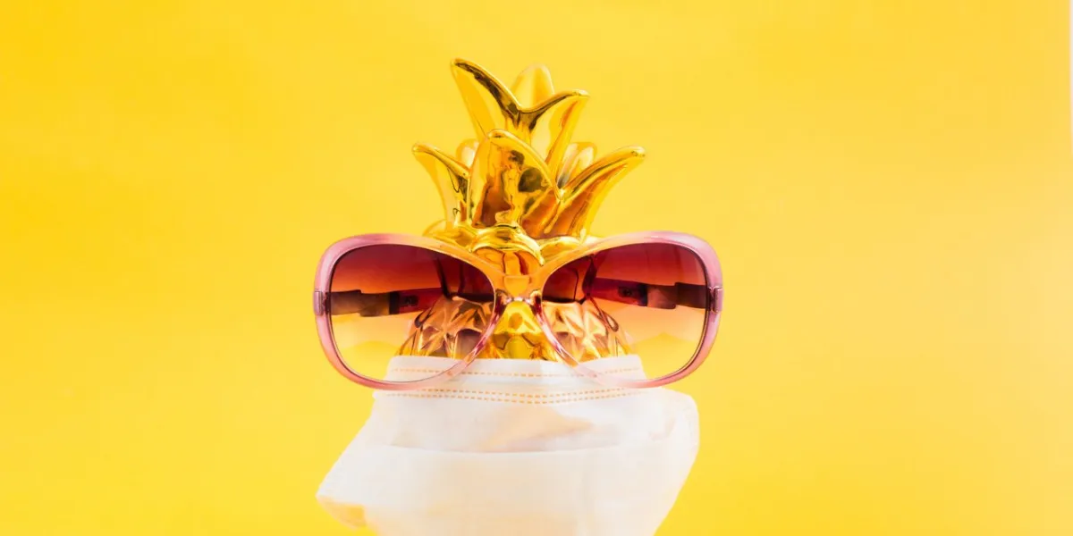 golden pineapple with pink sunglasses and medicine face mask on yellow background summer vacation concept with vatamin and prevention of viruses