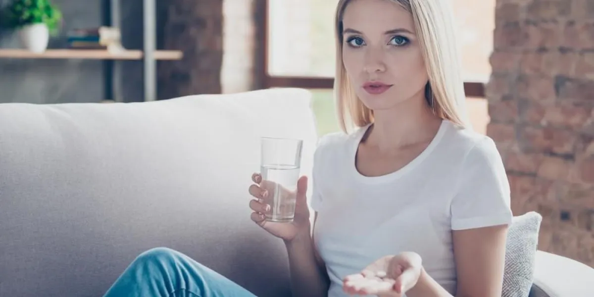 sad unhappy depressed woman is holding a pill in a hand and a glass of water, she is very ill and stayed at home instead of going to work