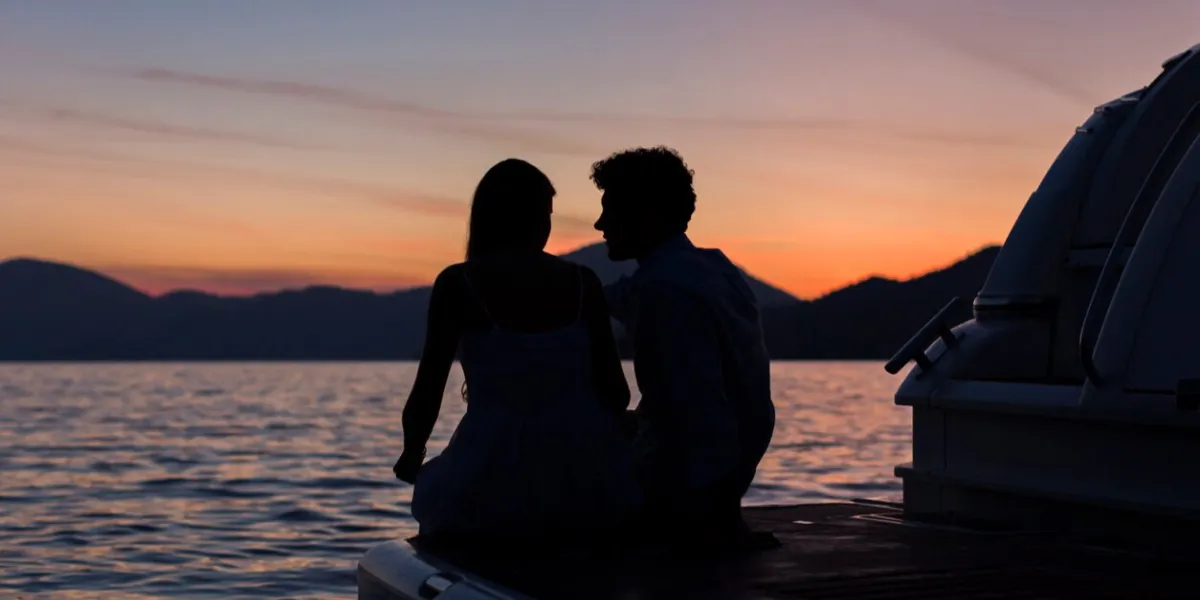 young couple sitting on stern of yacht at amazing sunset
