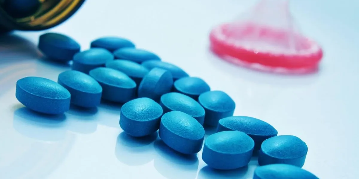 a pile of blue pills coming out of a bottle and a condom in the background