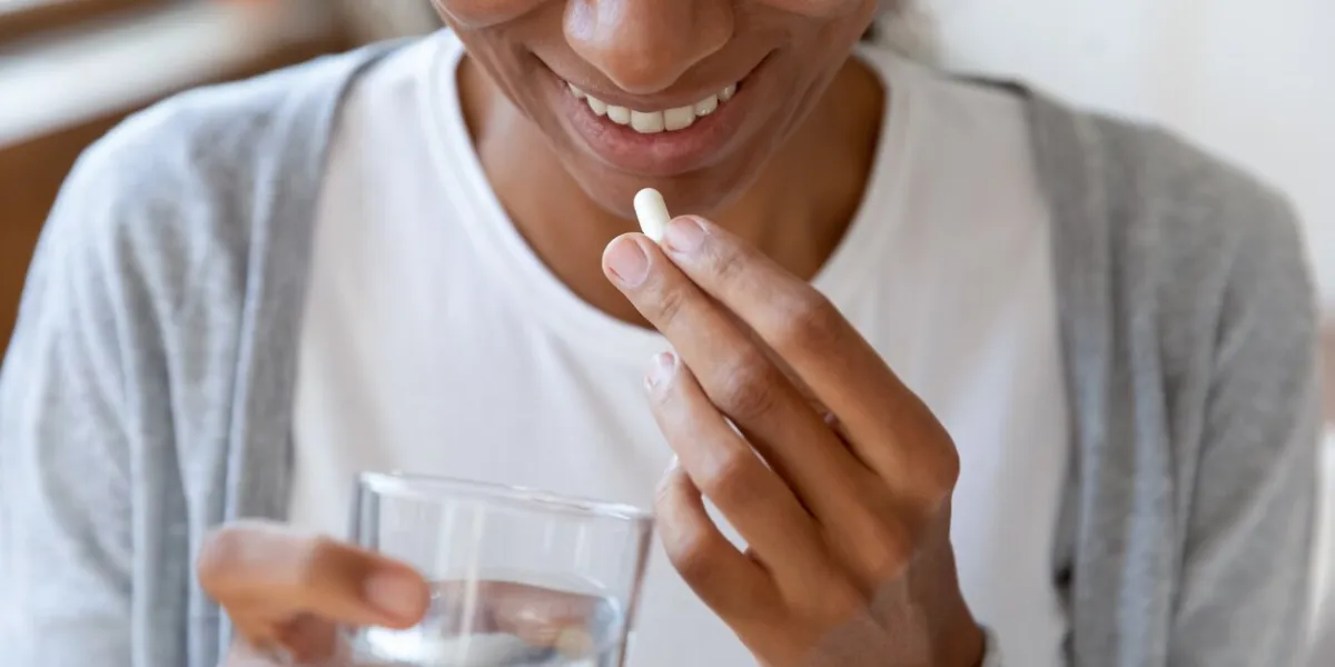 close up happy young african american young woman taking daily dose of complex healthcare skin, hair and nails omega vitamins drinking glass of fresh pure water, immunity improvement concept