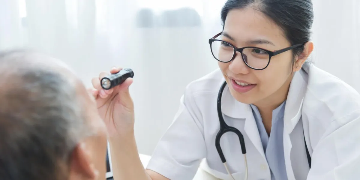 young asian female doctor wear glasses checking senior man patient eyes with flashlight in medical office