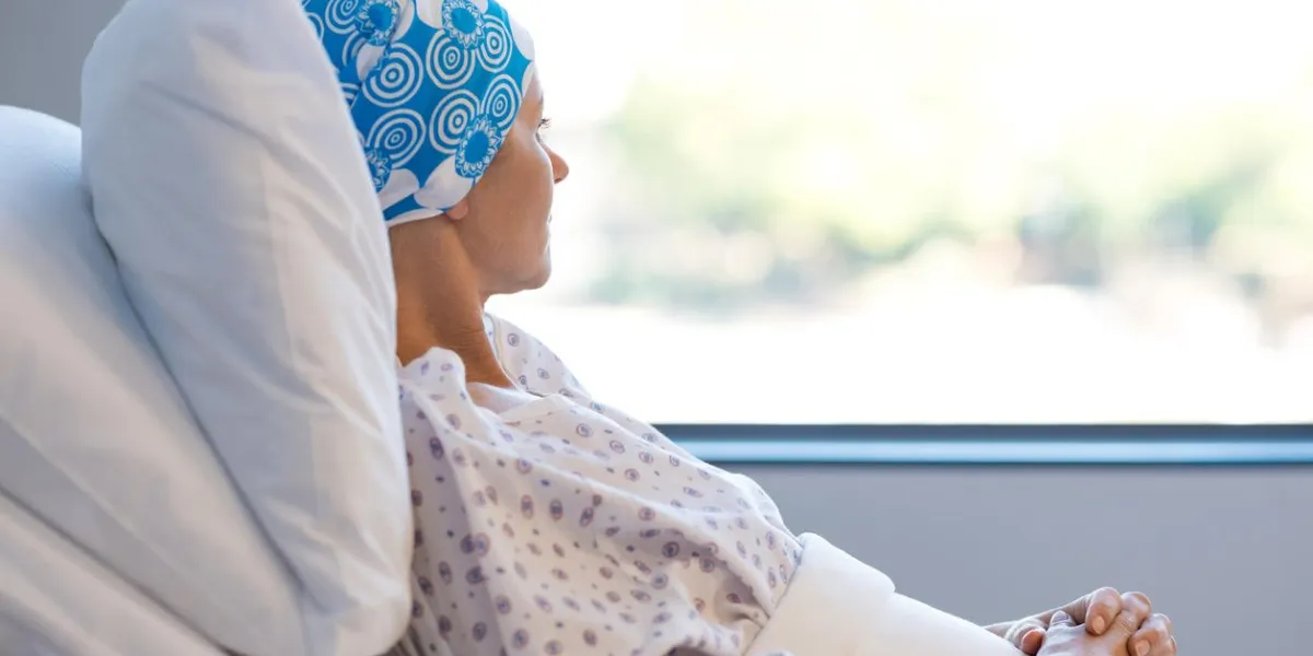 young woman in bed suffering from cancer thoughtful woman battling with tumor looking out of window young patient with blue headscarf recovery in hospital on bed
